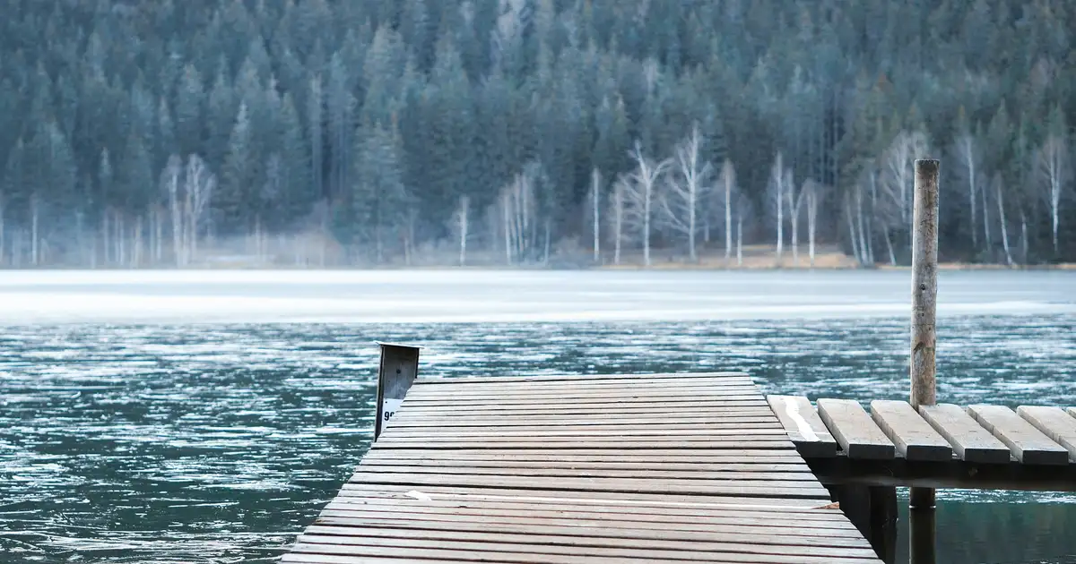 A wooden dock extending into a calm Ontario lake with a motorboat tied alongside at sunset