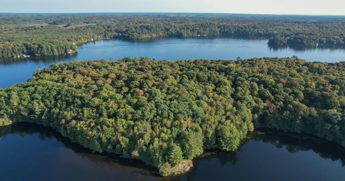 A cottage on a rocky Canadian Shield shoreline in the Haliburton Highlands with autumn foliage reflected in calm water