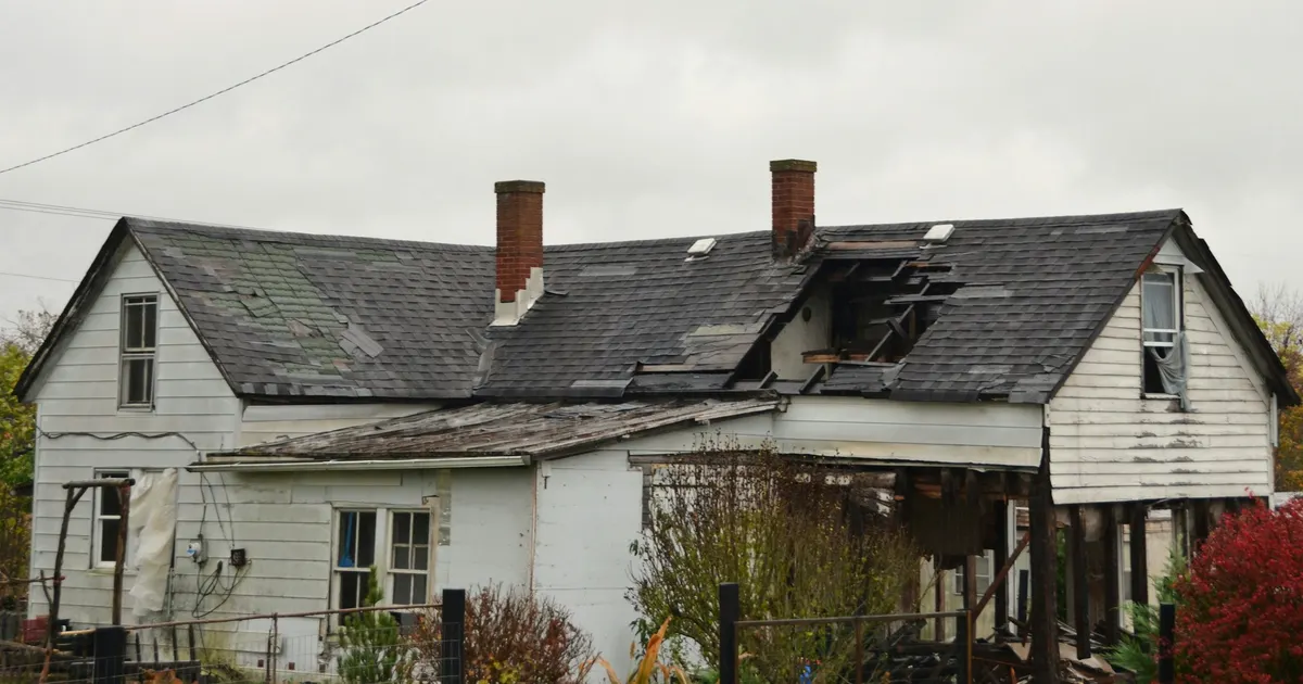 An insurance adjuster with a clipboard inspecting exterior damage to an Ontario cottage after a storm