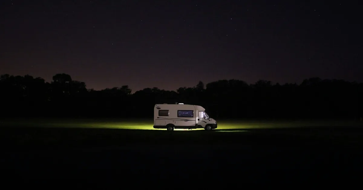 A Class A motorhome parked at a lakeside Ontario campground surrounded by pine trees on a sunny afternoon