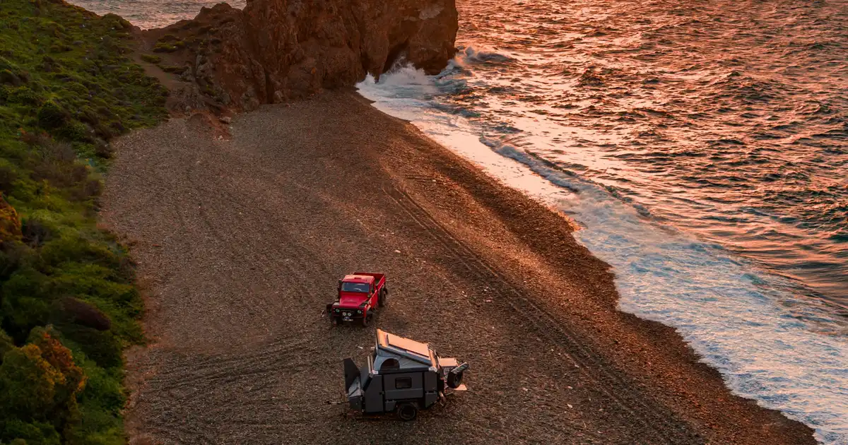 A travel trailer parked beside a Canadian motorhome at an Ontario campground with picnic table and fire ring