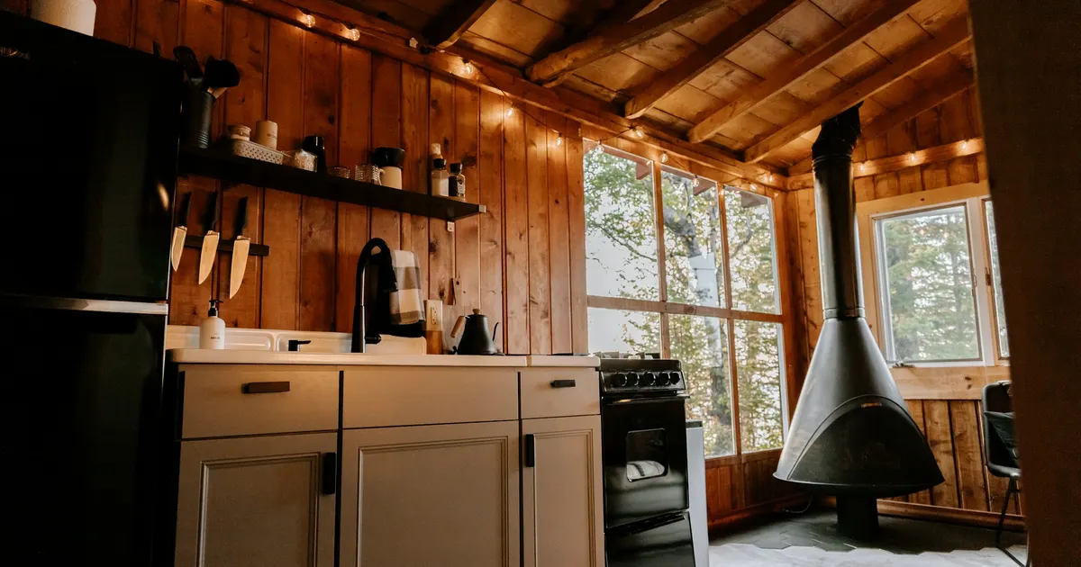 A cast iron wood stove burning in a cozy Ontario cottage interior with stone hearth and pine walls